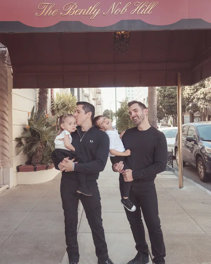 Two dads holding their son and daughter beneath the awning of their Nob Hill apartment building