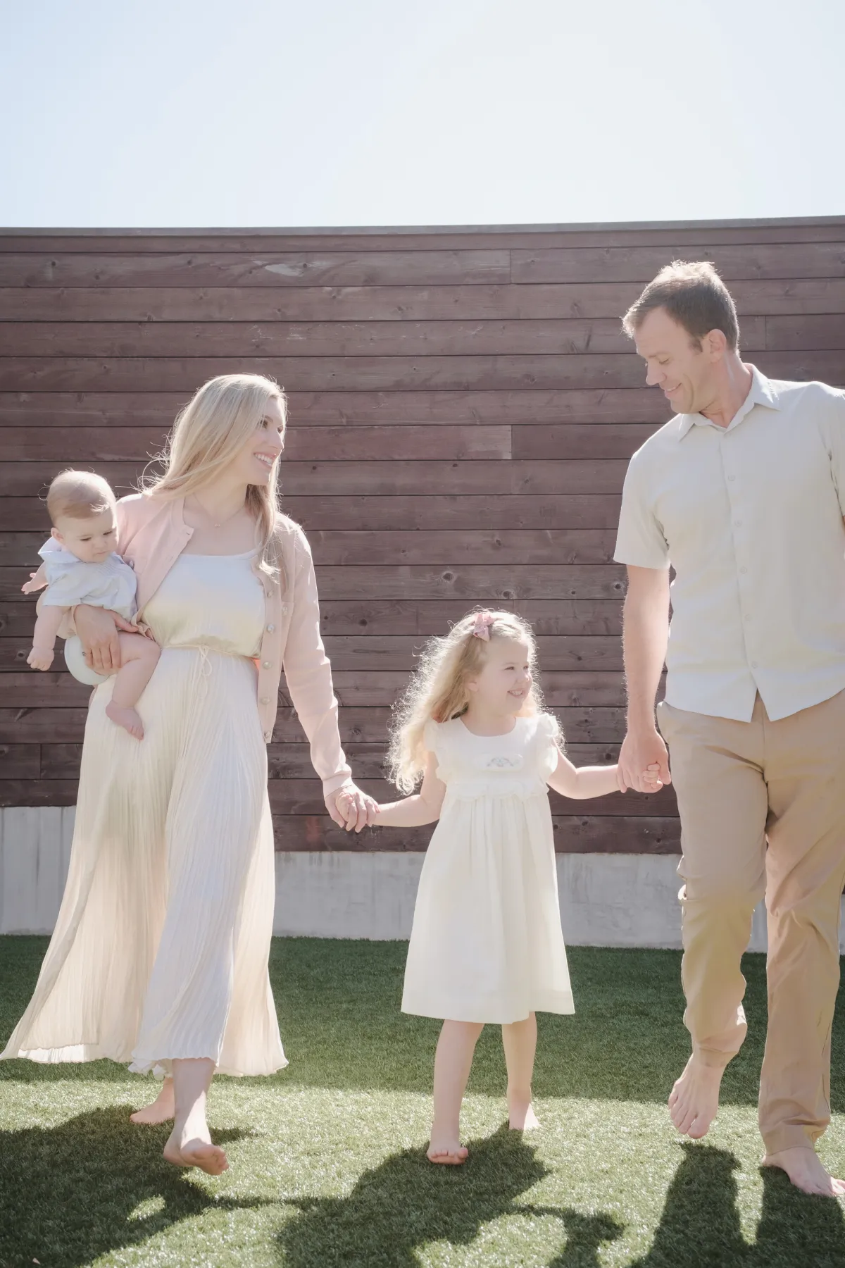 Family walking barefoot across their backyard holding hands, baby on mom's hip