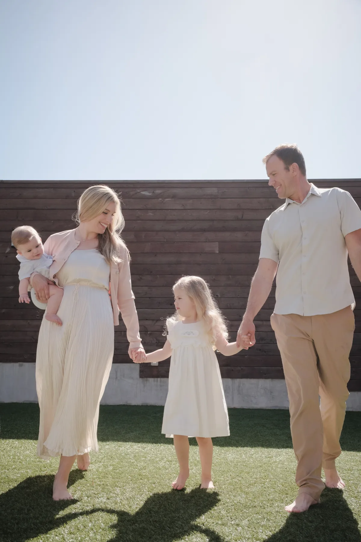 Parents and daughter holding hands in the sun in front of a tall wood fence