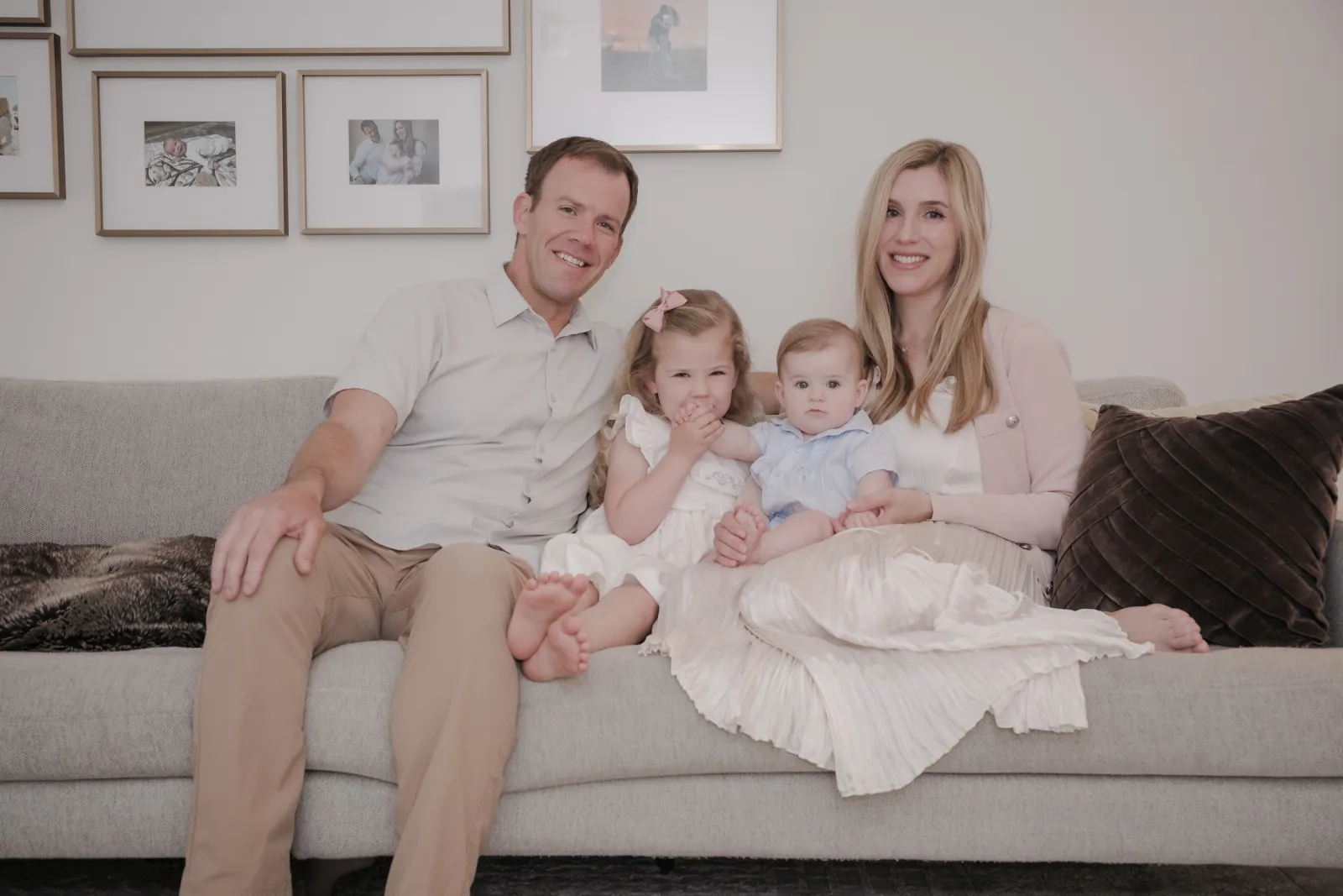 Family of four on a grey sofa beneath a gallery wall of framed photos in their San Francisco home