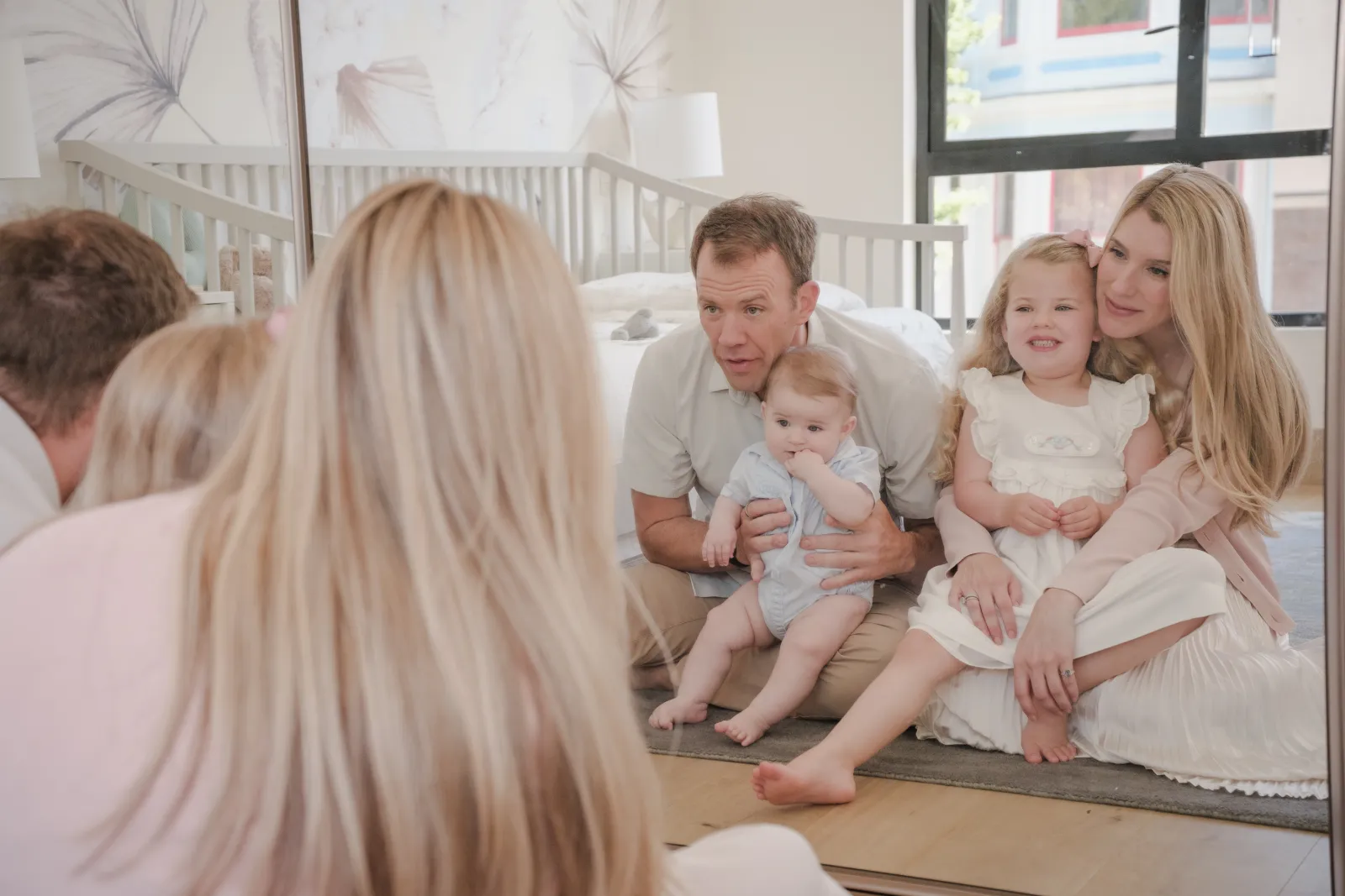 Father talking to his baby son while his daughter sits in her mother's lap, seen in a mirror