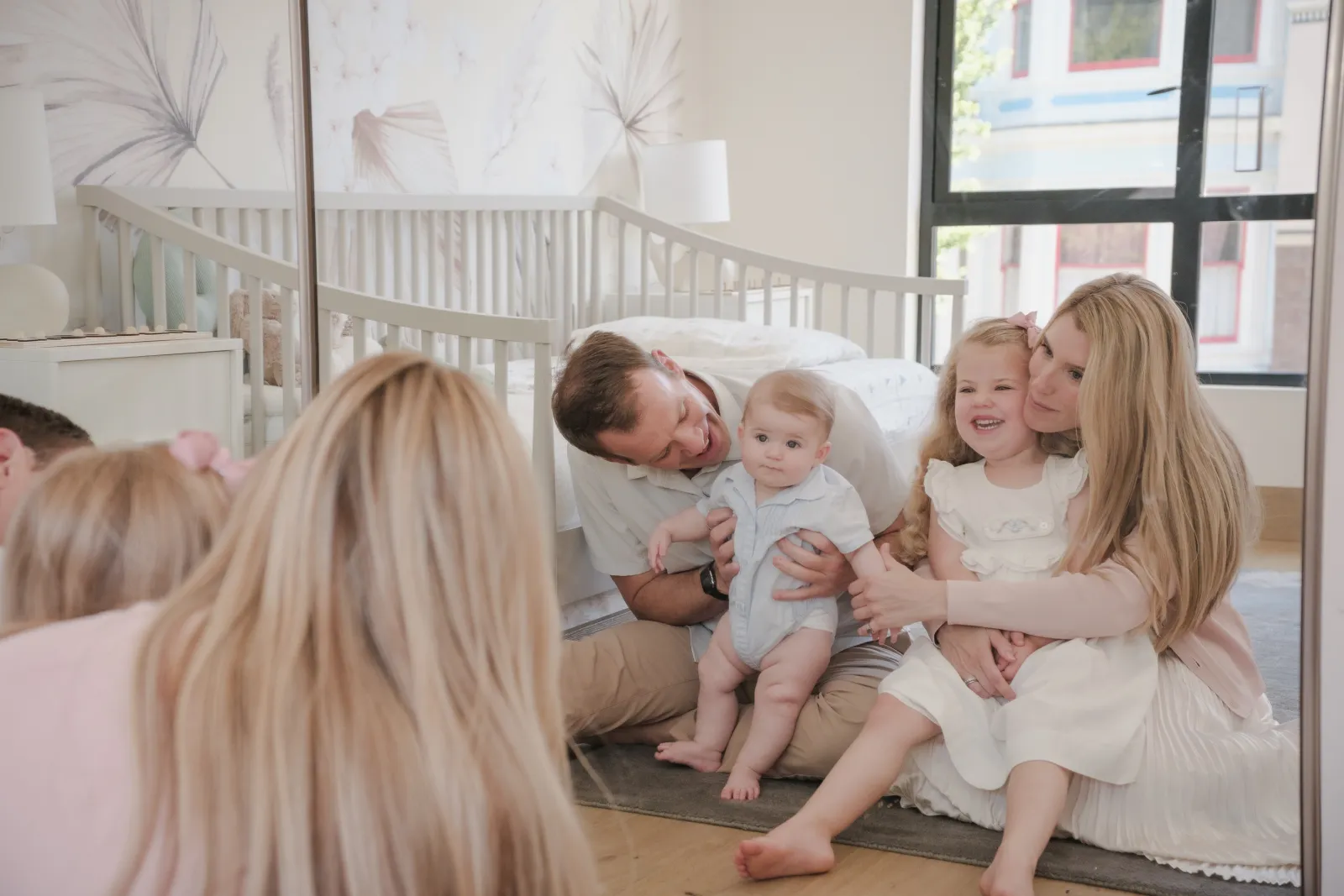 Dad laughing with his baby as mom and daughter press cheeks together in the nursery mirror