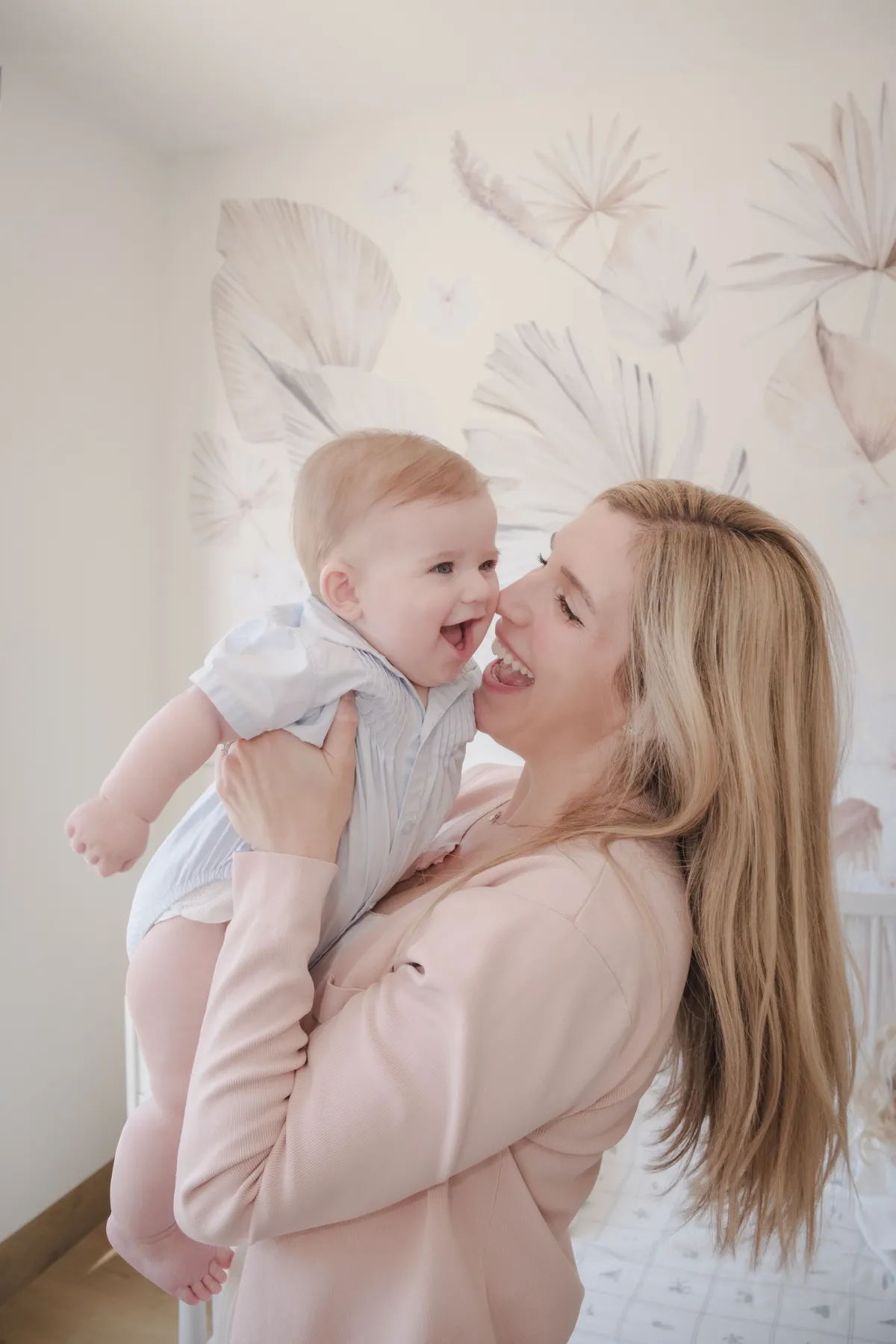 Mother lifting her laughing baby son nose to nose in his nursery