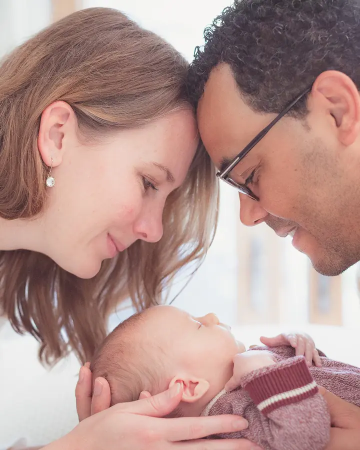 Parents touching foreheads above their newborn baby during an in-home session