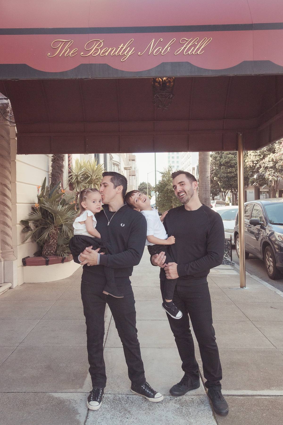 Two dads holding their son and daughter beneath the awning of their Nob Hill apartment building