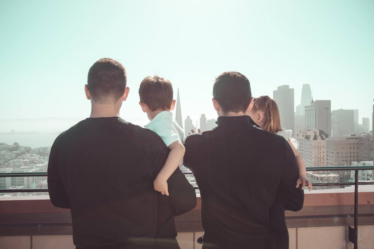 Two dads holding their children on the rooftop, looking out at the downtown skyline