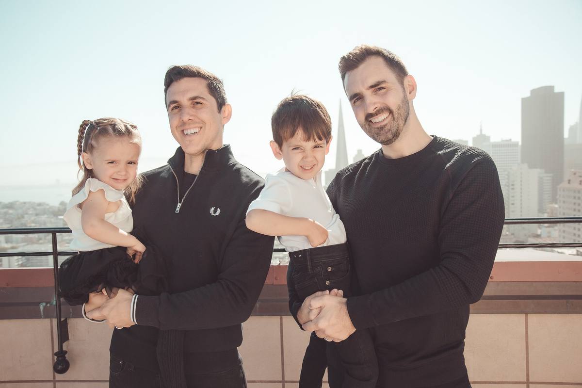 Two dads smiling with their children on the rooftop with the city skyline behind them