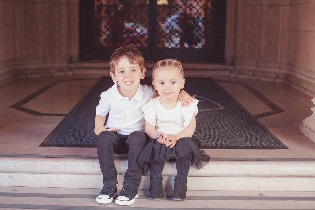 Brother and sister sitting together on the marble entry steps of their building