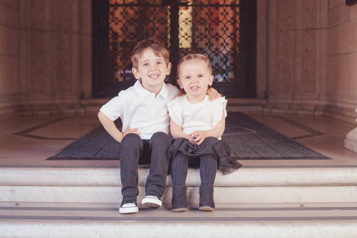 Brother and sister smiling side by side on the steps beneath the arched doorway