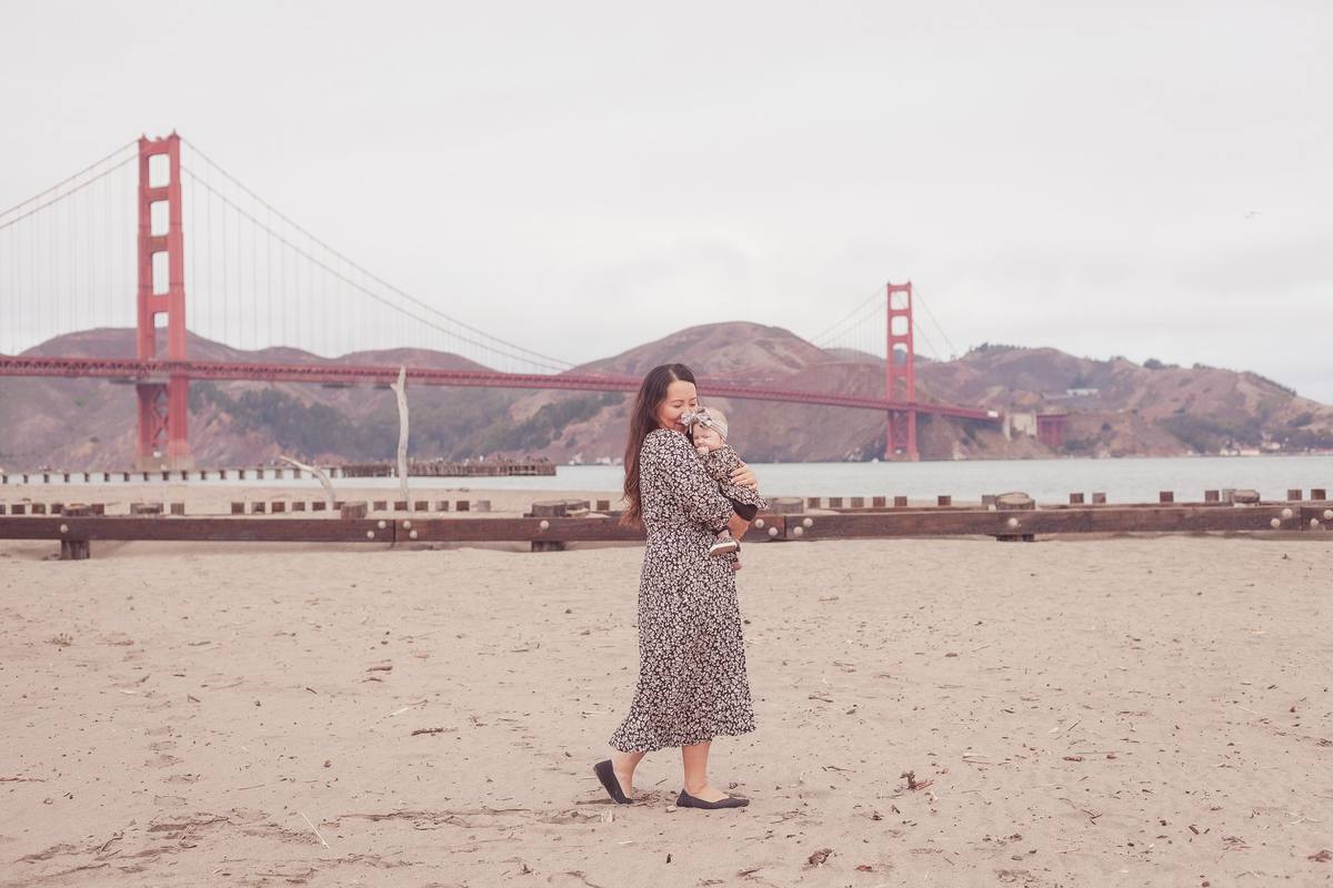 Mother holding her baby daughter on the beach at Crissy Field with the Golden Gate Bridge behind them