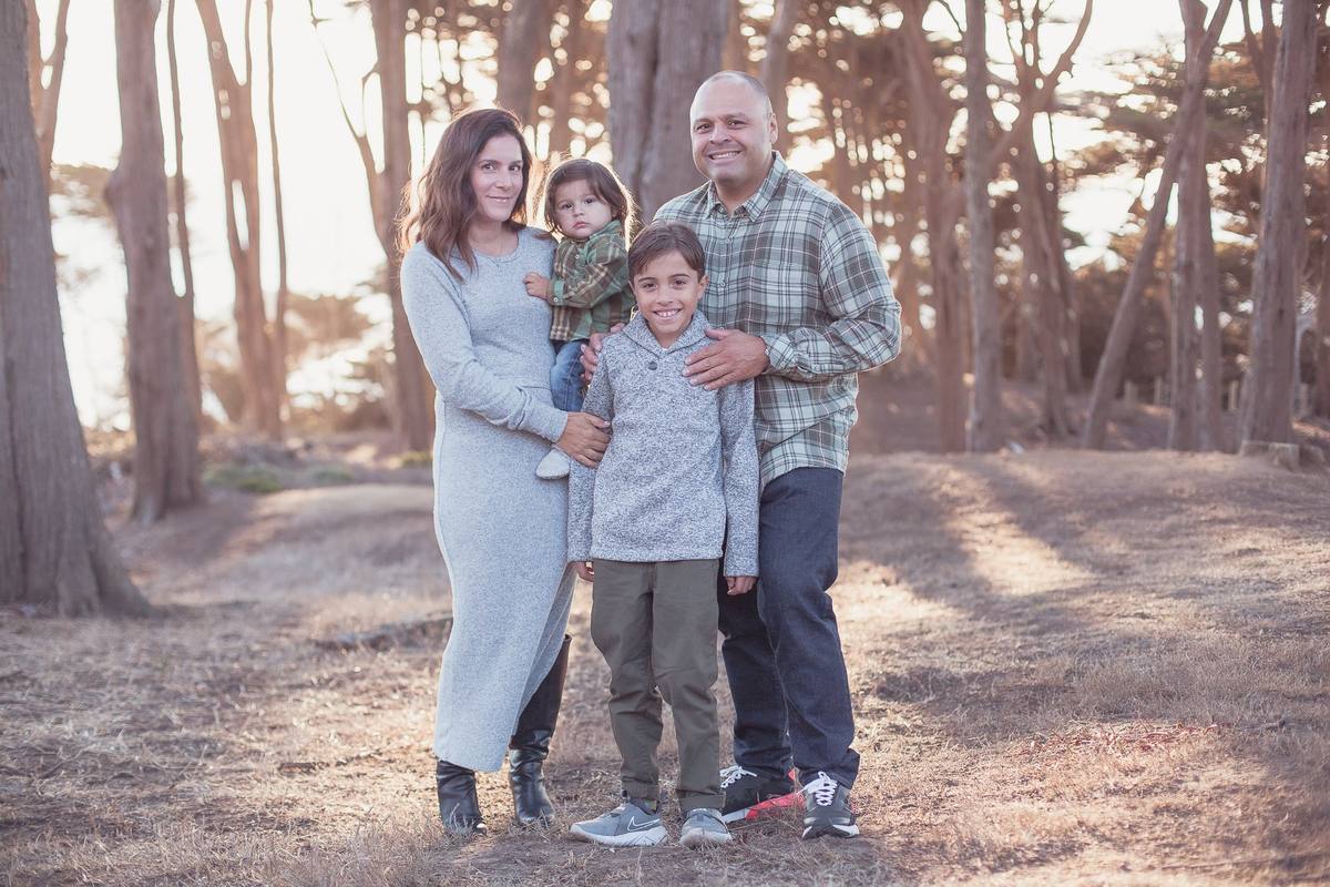 Family of four standing among the cypress trees in golden light at Lands End