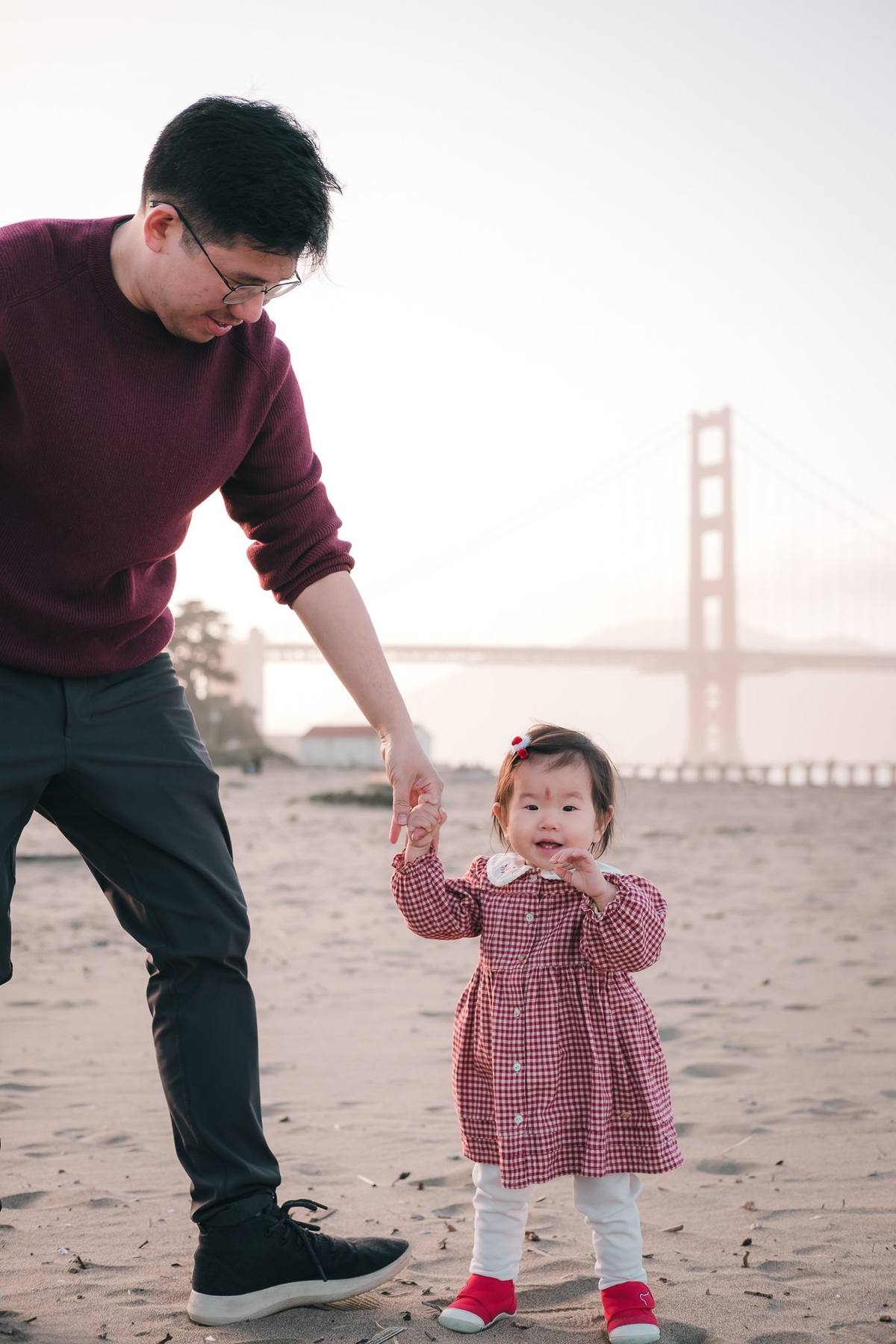 Father holding his baby daughter's hand as she toddles across the beach at Crissy Field
