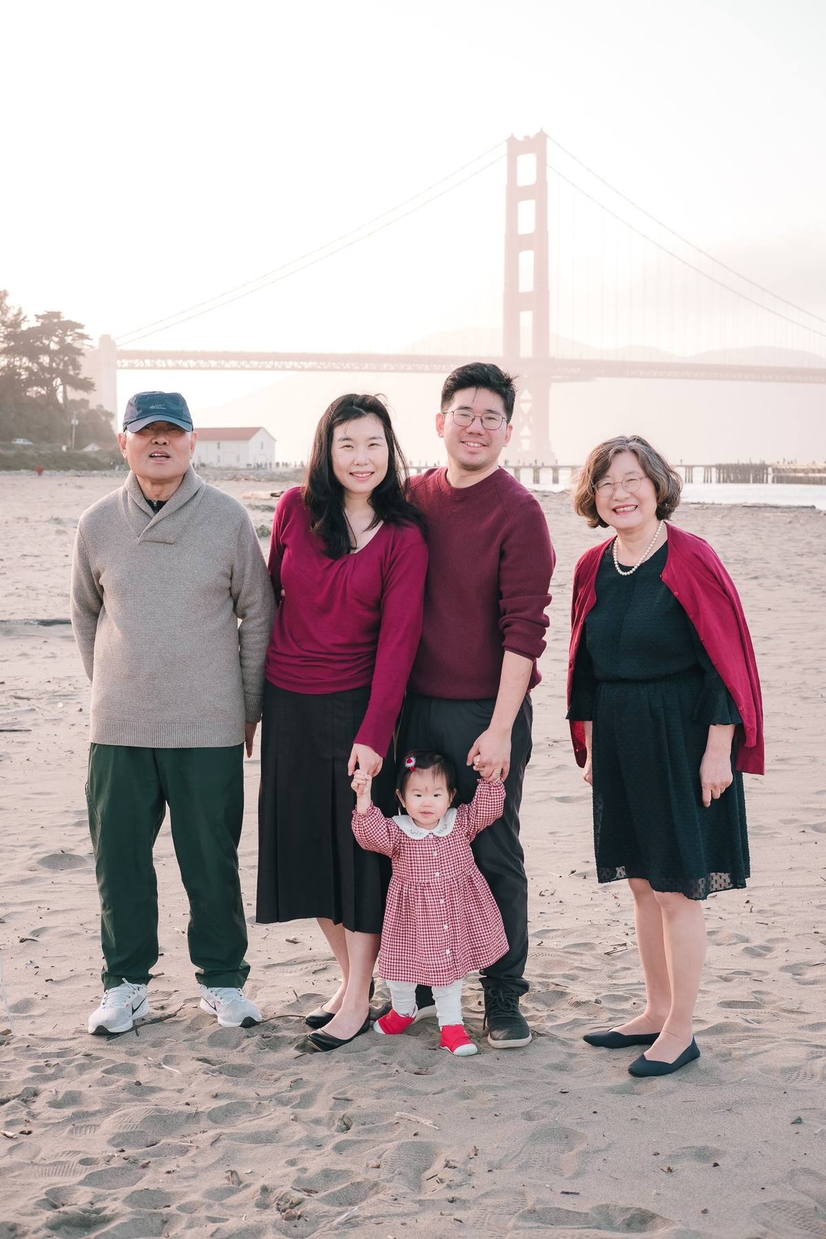 Grandparents, parents, and baby girl in coordinated burgundy and black on the beach at Crissy Field
