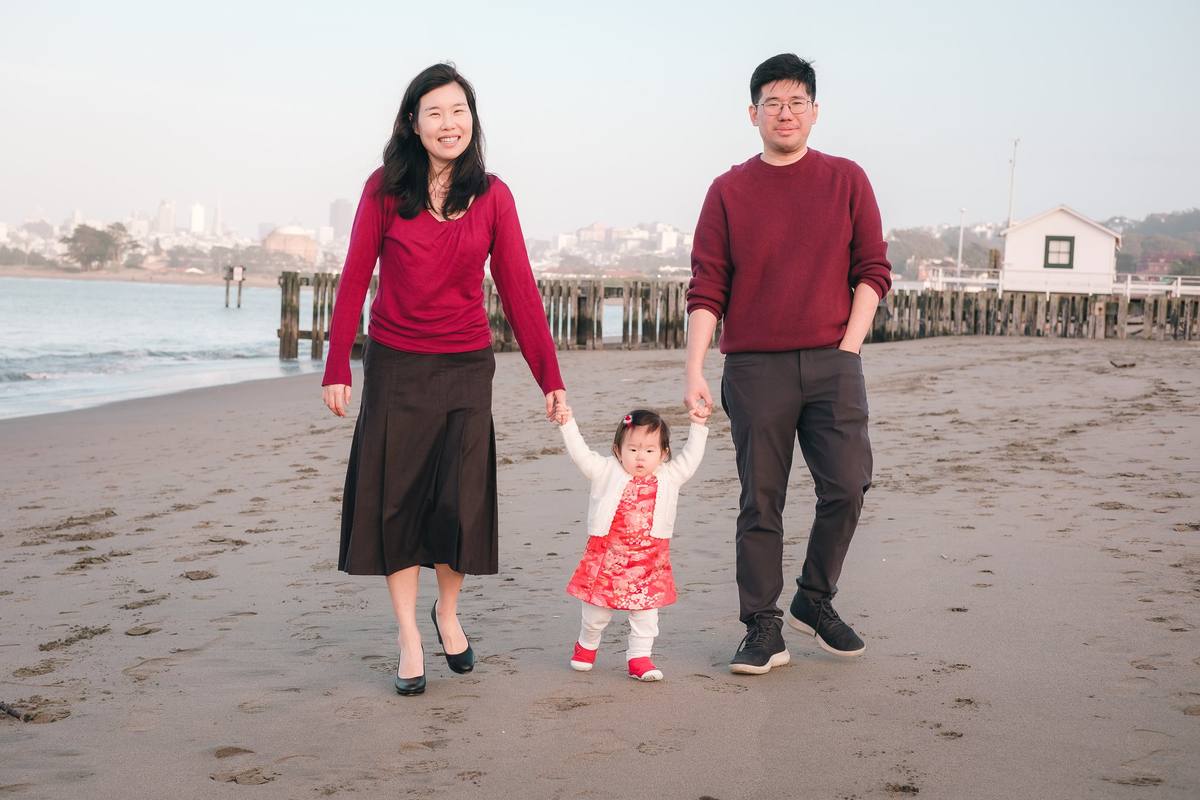 Parents walking their baby girl along the shoreline at Crissy Field with the pier behind them