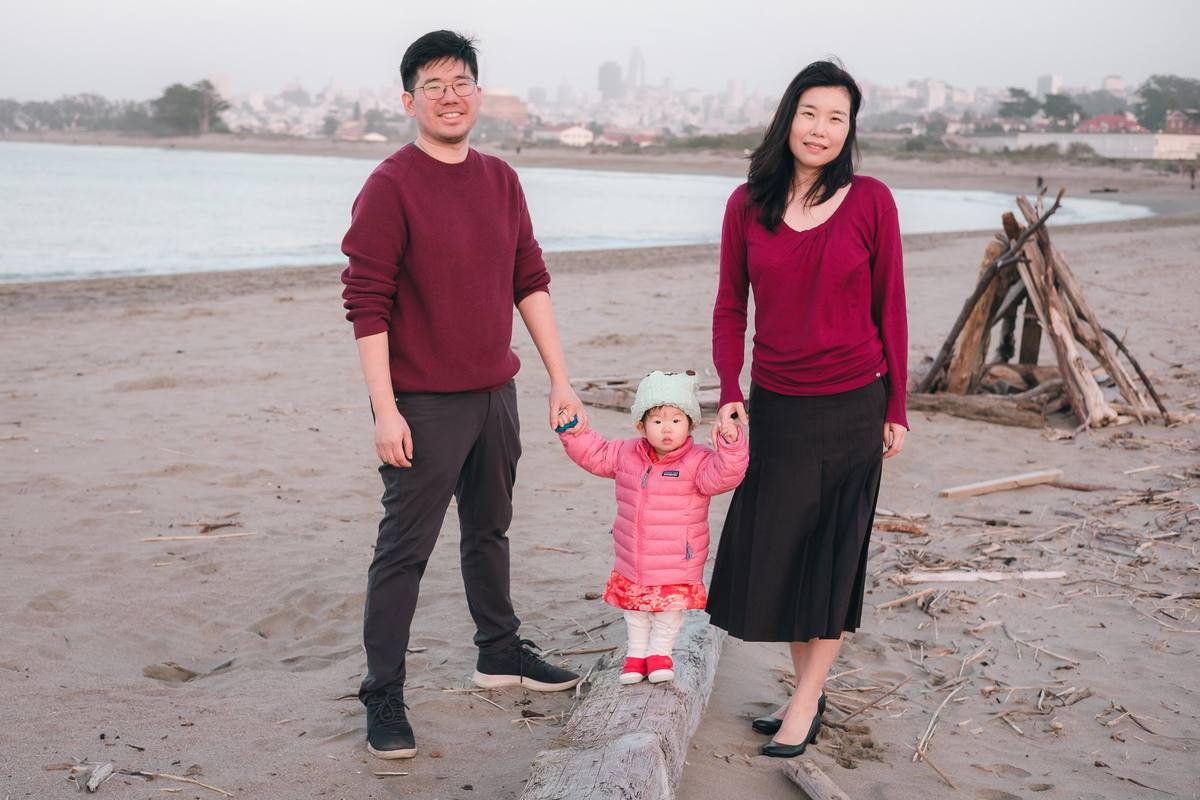 Parents holding their baby girl's hands on a driftwood log at Crissy Field beach