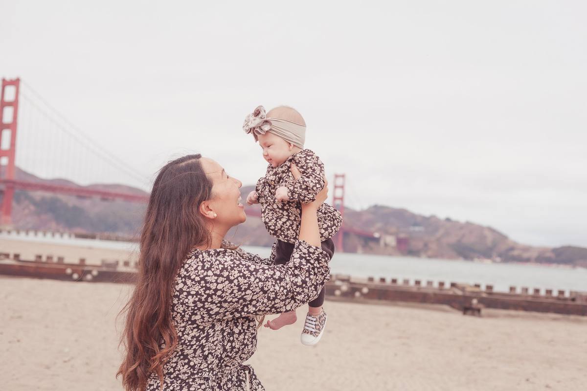 Mother lifting her baby daughter into the air with the Golden Gate Bridge in the background
