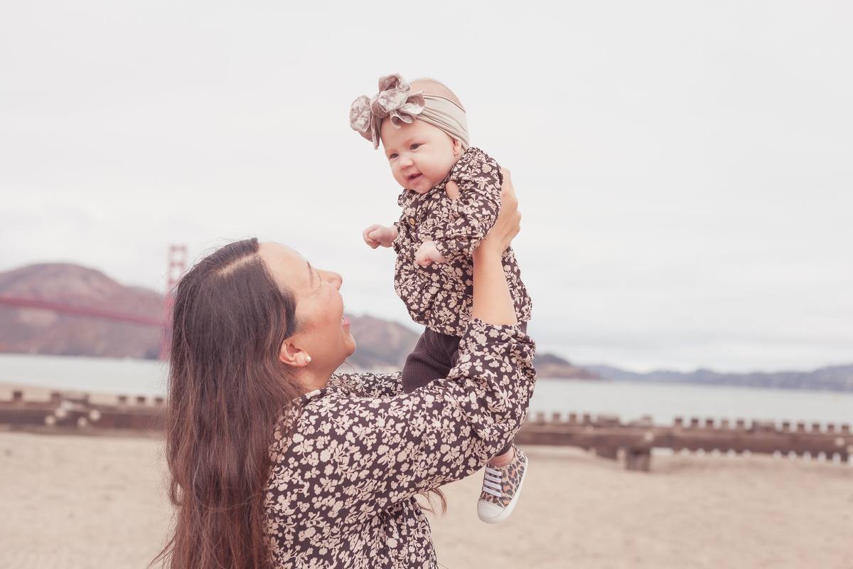 Mother smiling up at her baby daughter held overhead on the beach at Crissy Field