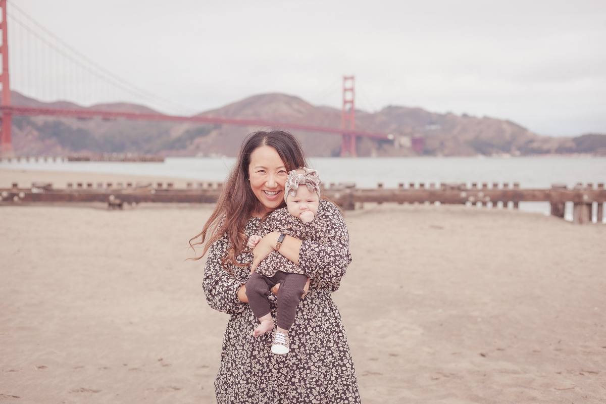 Mother hugging her baby daughter in matching floral outfits on the beach at Crissy Field