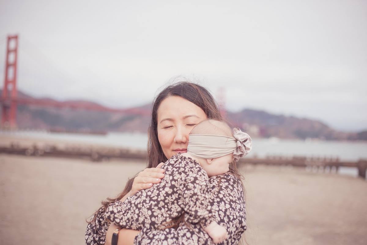 Mother with her eyes closed holding her baby daughter close by the bay at Crissy Field