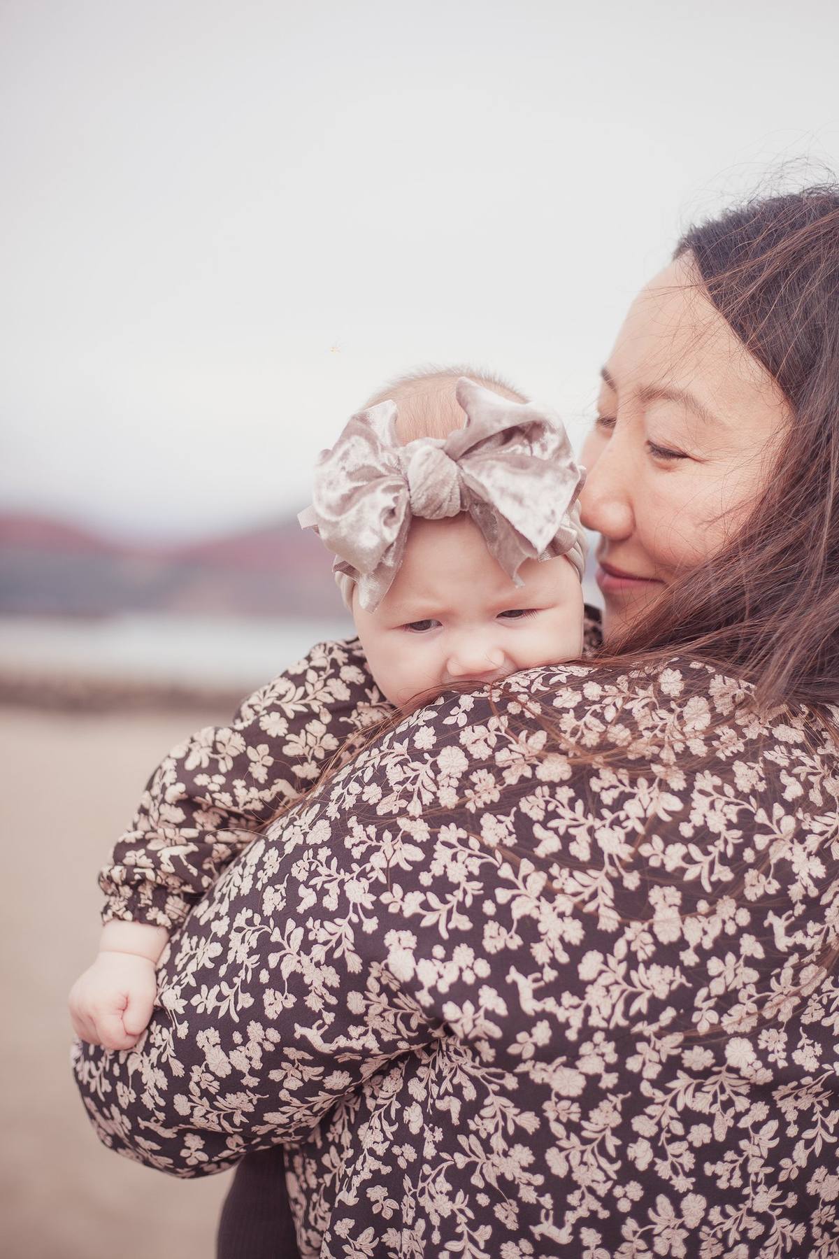 Close portrait of a baby girl in a floral bow resting on her mother's shoulder