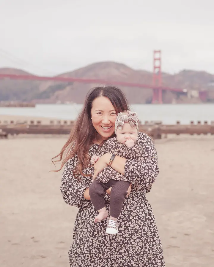 Mother hugging her baby daughter in matching floral outfits on the beach at Crissy Field