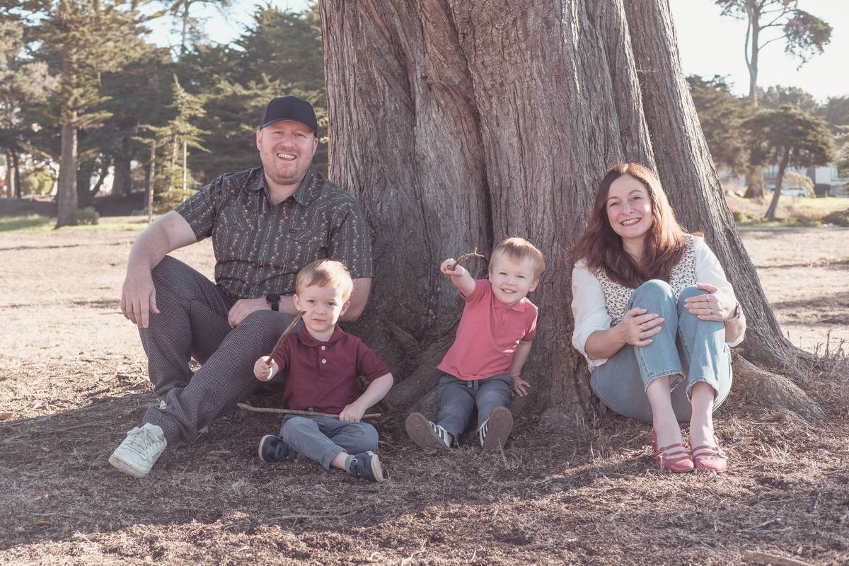 Family of four sitting at the base of a big cypress tree at Sutro Park