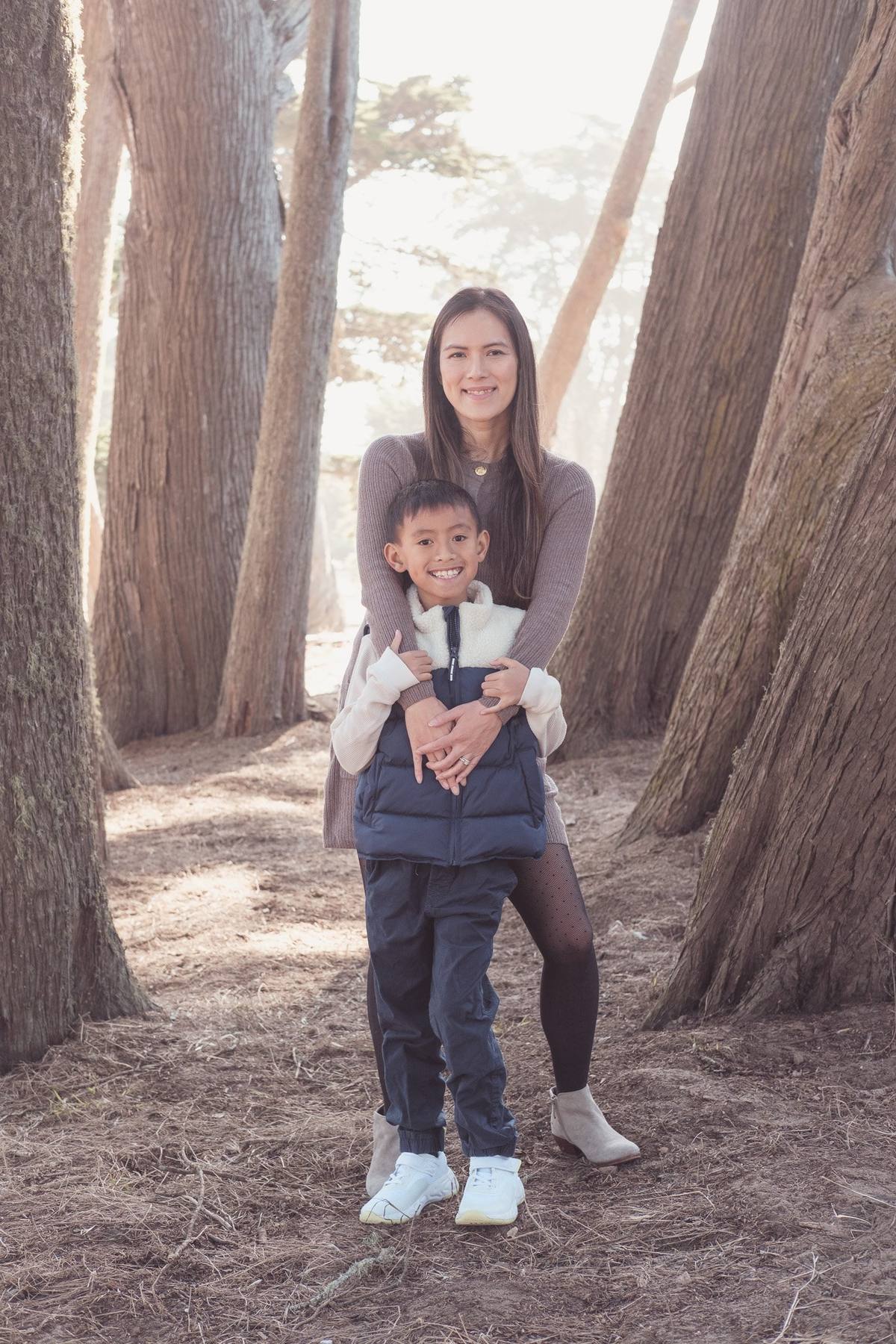 Mother hugging her son from behind among the cypress trunks at Sutro Park