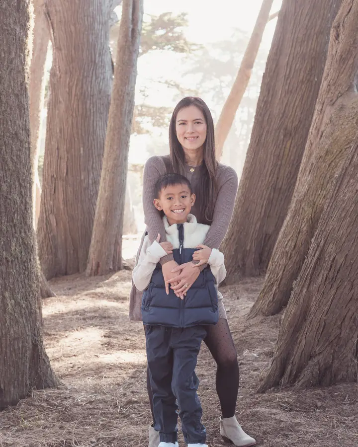 Mother hugging her son from behind among the cypress trunks at Sutro Park