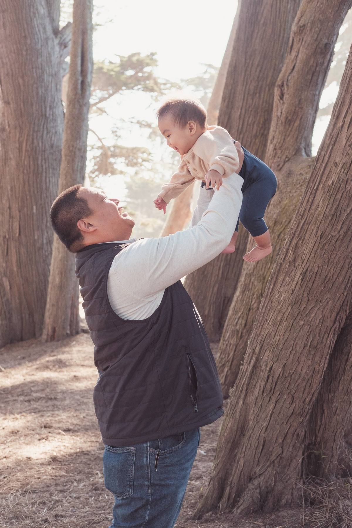 Father lifting his laughing baby overhead among the cypress trees at Sutro Park