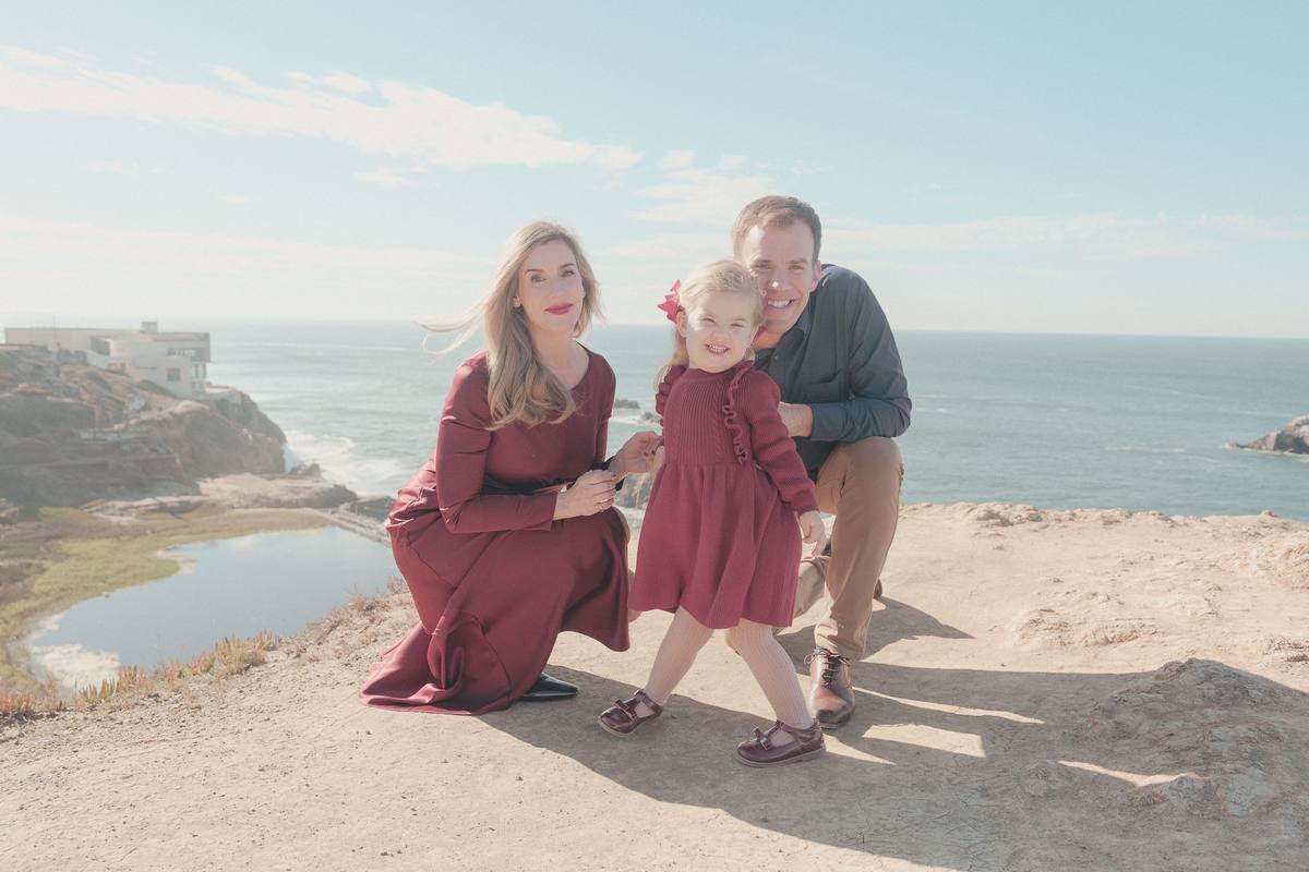 Family of three on the bluff at Lands End with the Sutro Baths ruins and the Pacific behind them