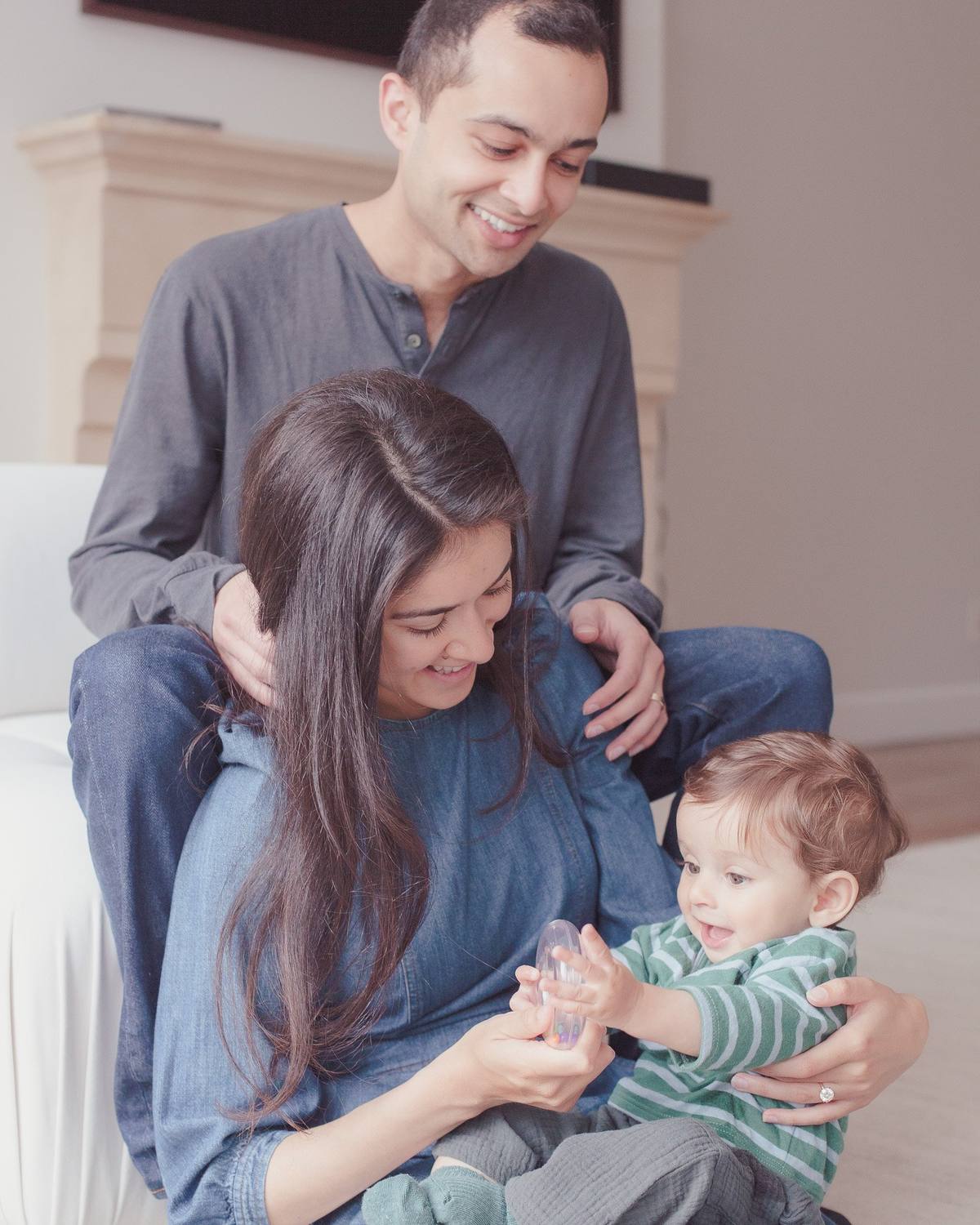 Mom and dad laughing on the living room floor as their baby plays in mom's lap