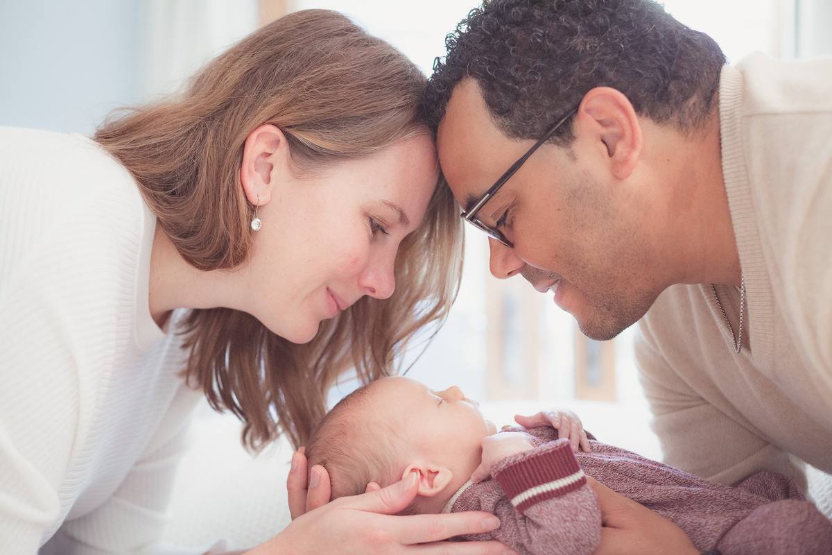 Parents touching foreheads above their newborn baby during an in-home session