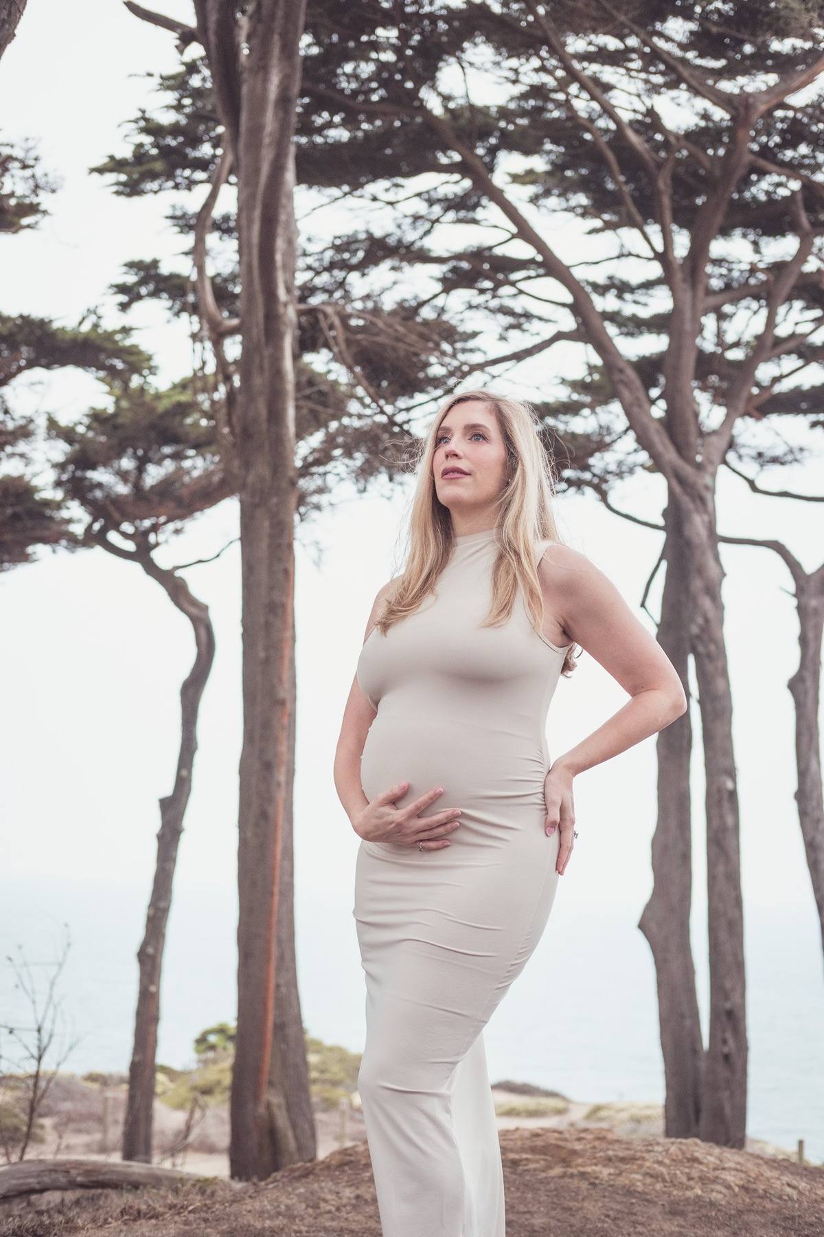 Pregnant mother looking out under the tall trees at Lands End on an overcast day