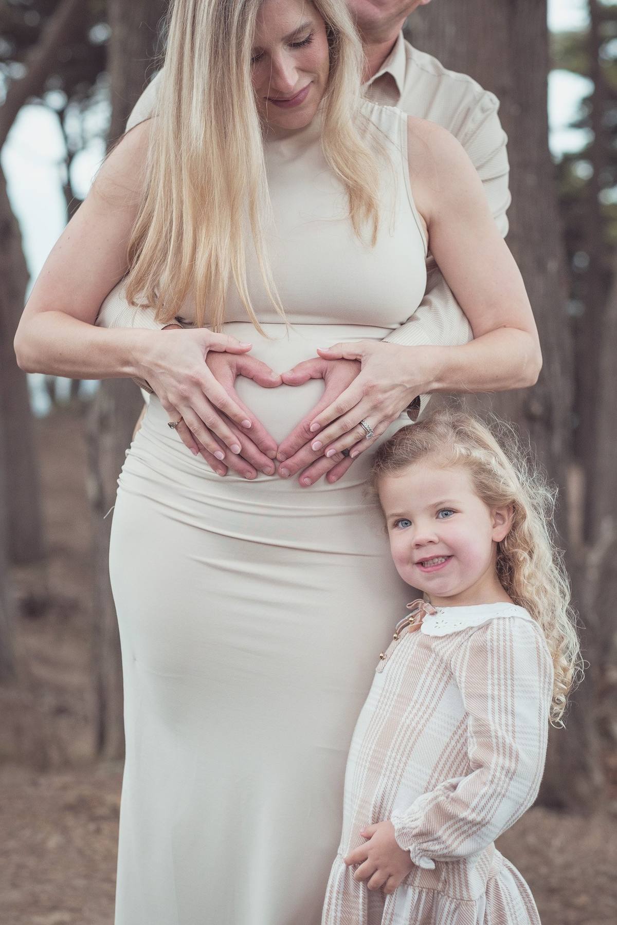 Mother making a heart with her hands over her bump as her daughter leans against her