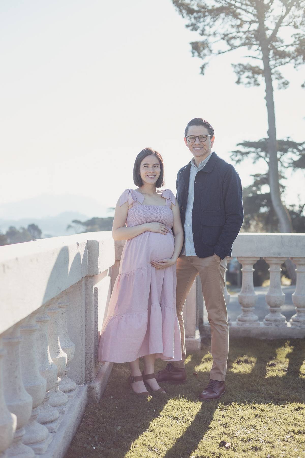 Expecting couple standing beside the stone balustrade at the Legion of Honor