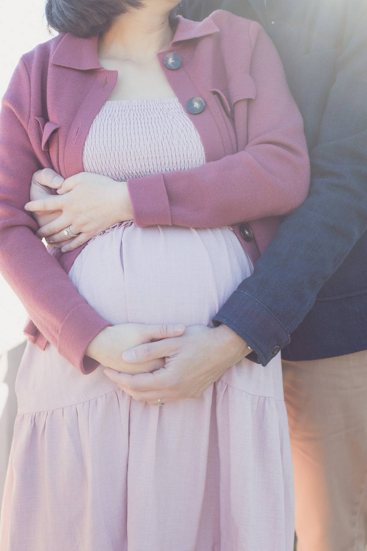 Close-up of a couple's hands resting together on her baby bump