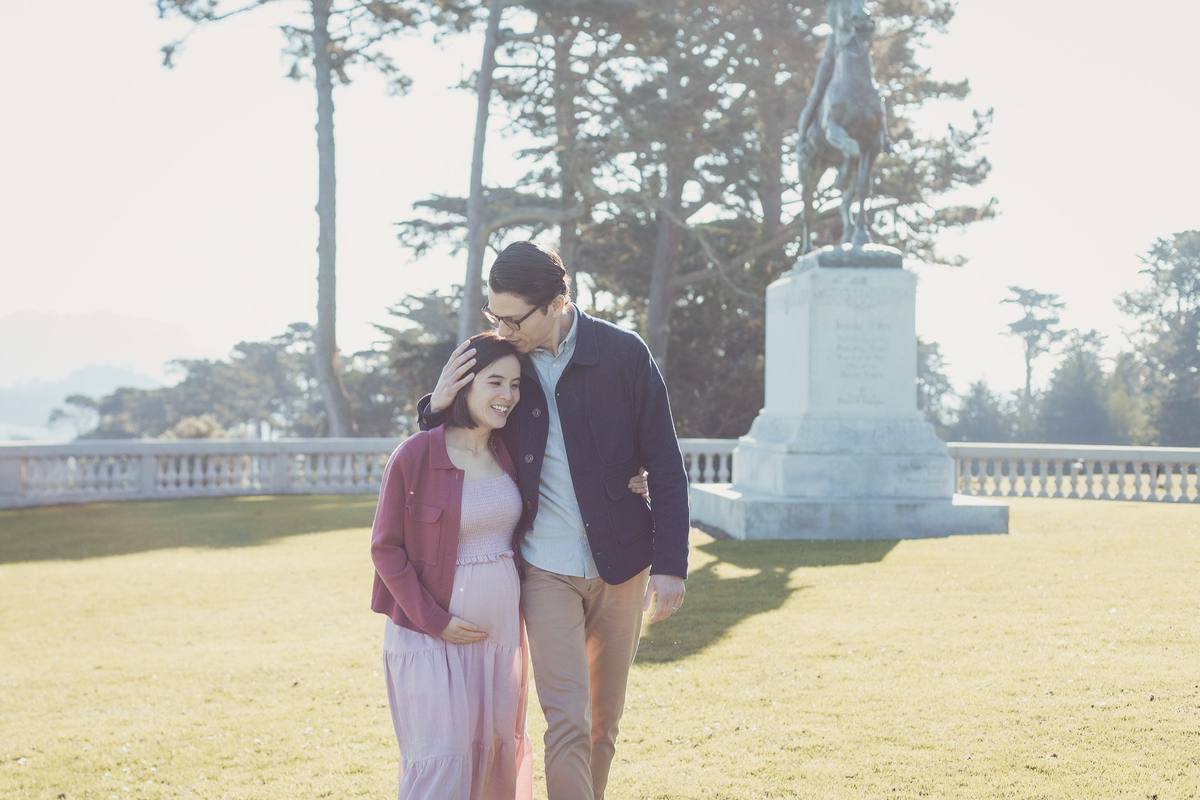 Expecting couple on the lawn at the Legion of Honor with a statue and cypress trees behind them