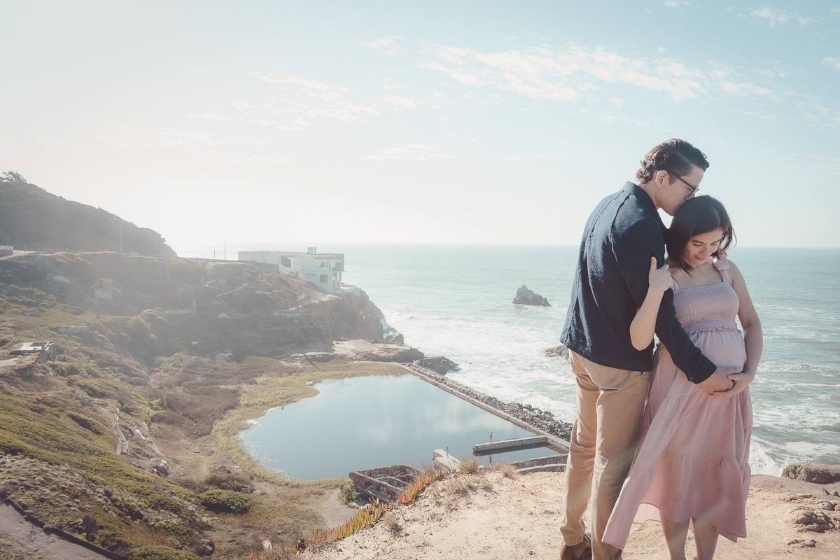 Expecting couple embracing on the cliffs at Lands End above the Sutro Baths ruins