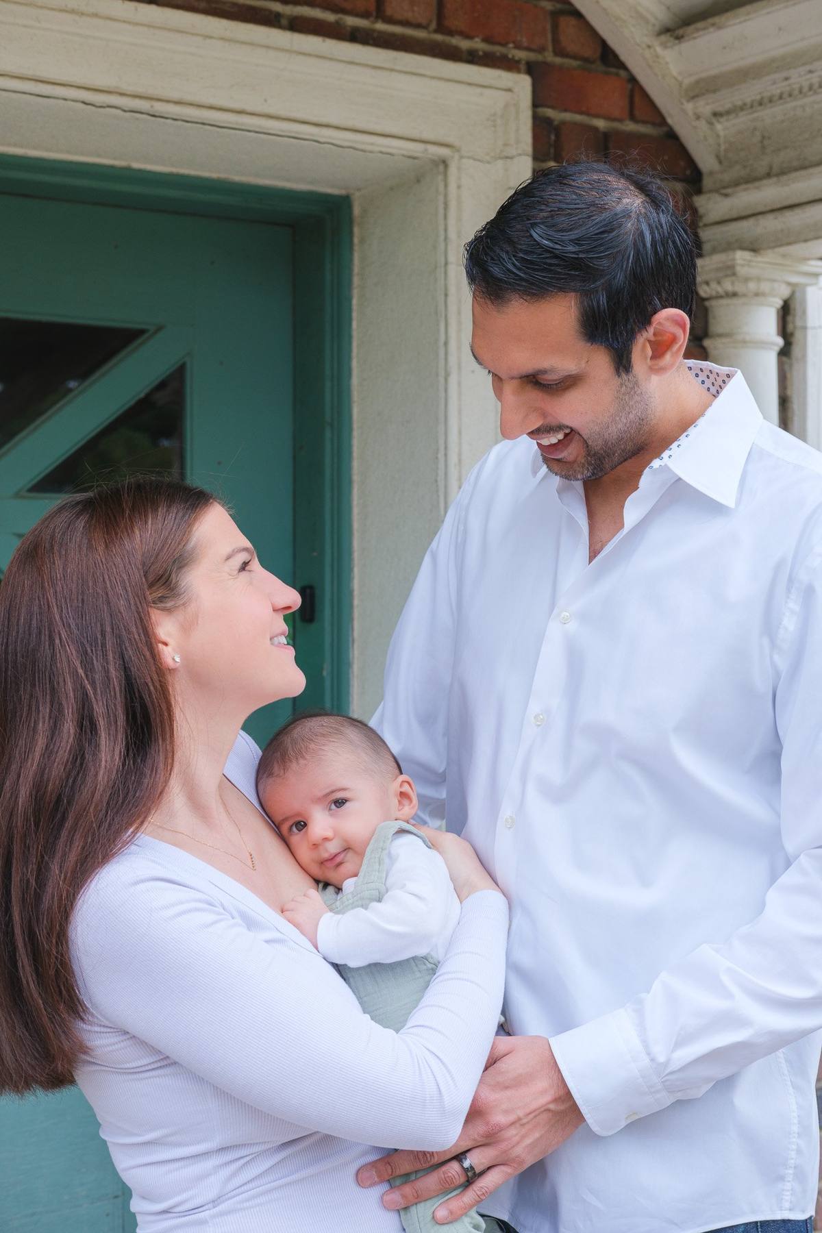 Parents smiling down at their baby son in front of a teal door at the Murphy Windmill
