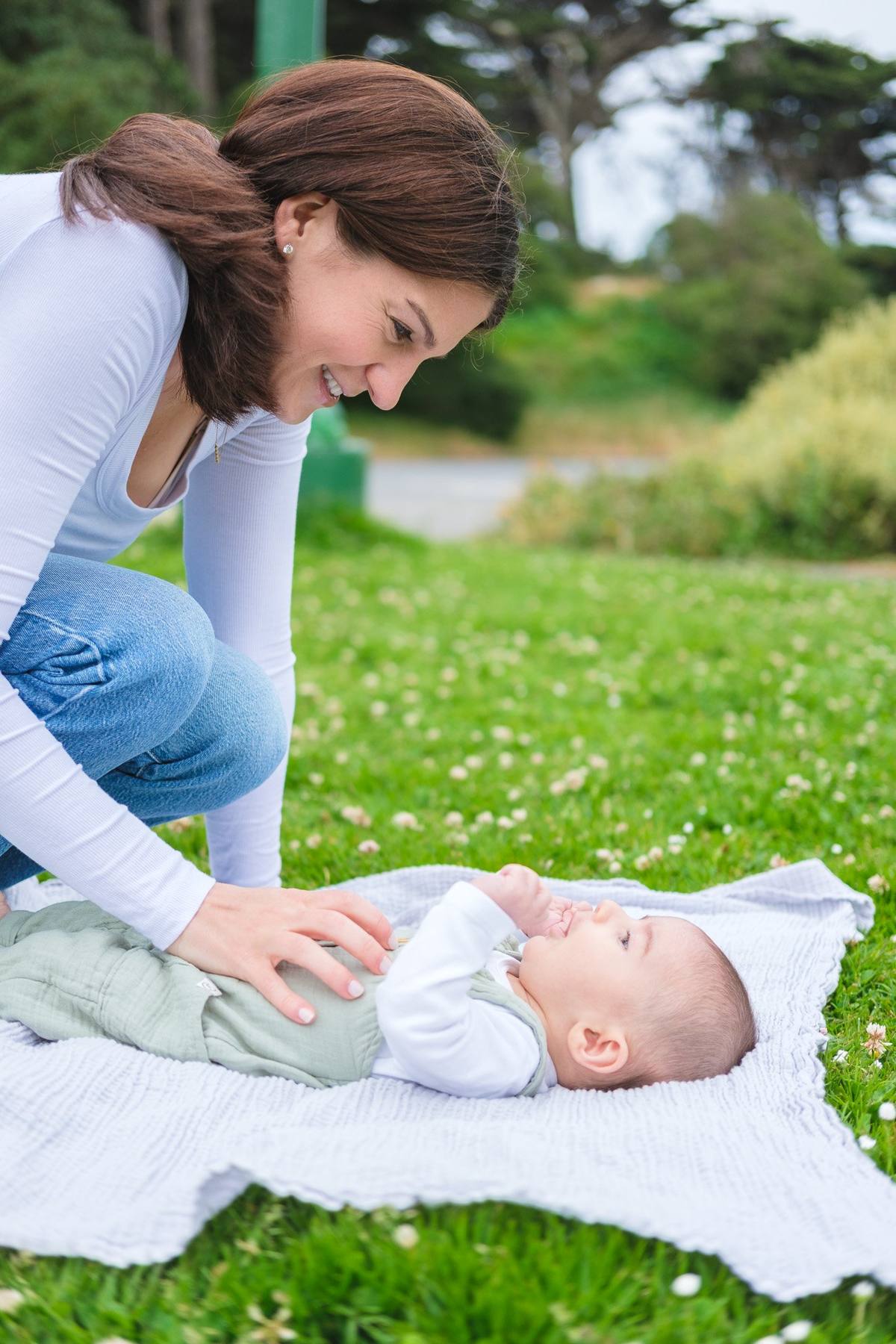 Mother leaning over her baby son lying on a blanket in the grass