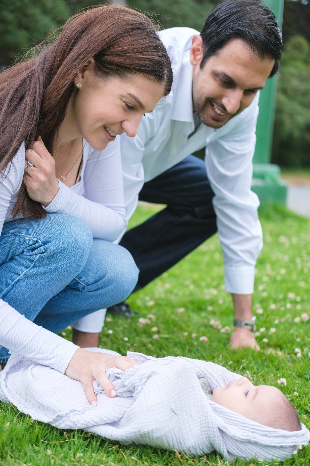 Parents crouching over their swaddled baby on a blanket on the lawn in Golden Gate Park