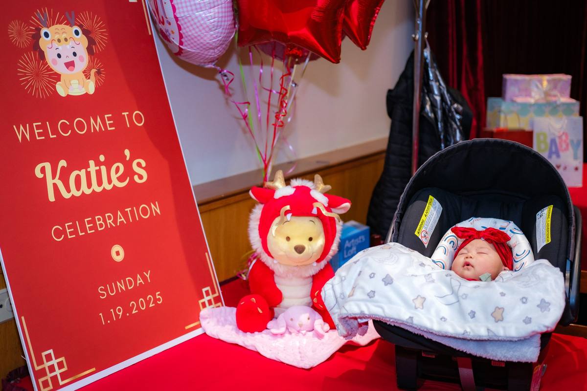 Sleeping baby in her car seat beside a welcome sign and a plush toy in a red dragon costume