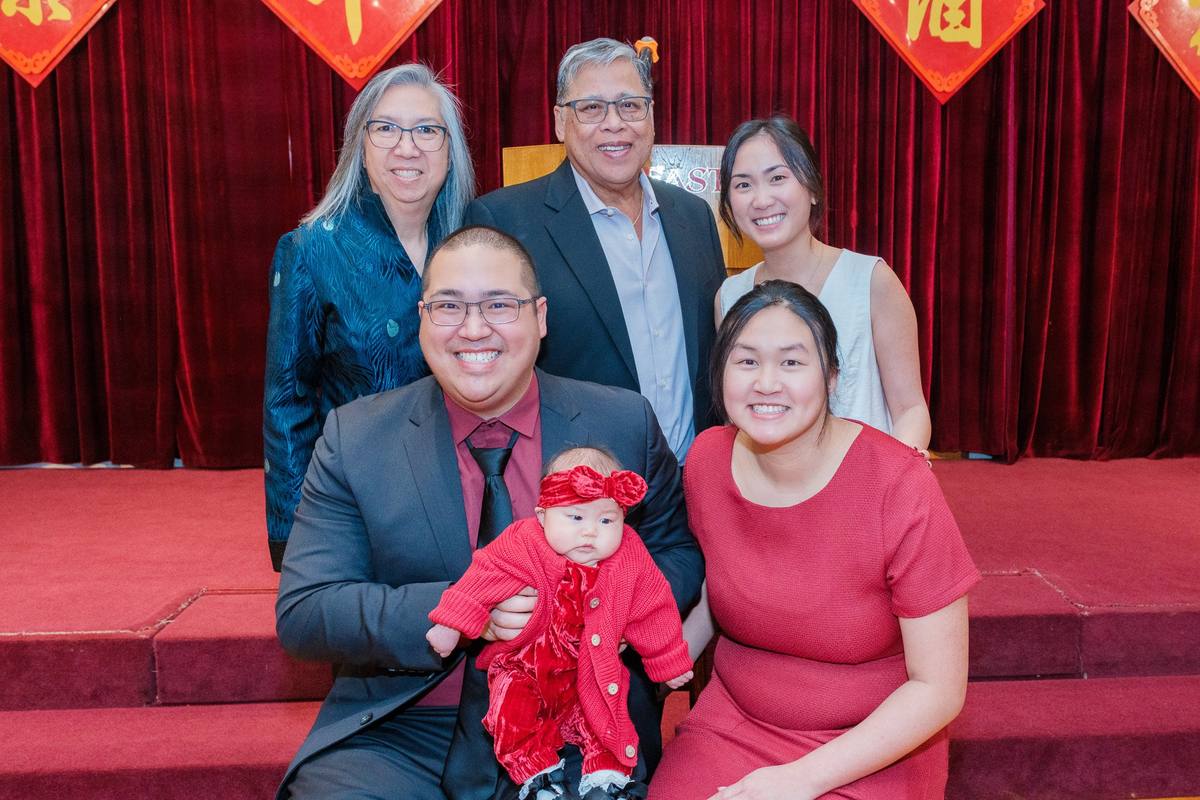 Three generations of the family posing with the baby in front of the banquet stage