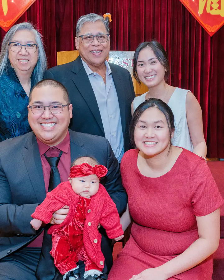 Three generations of the family posing with the baby in front of the banquet stage