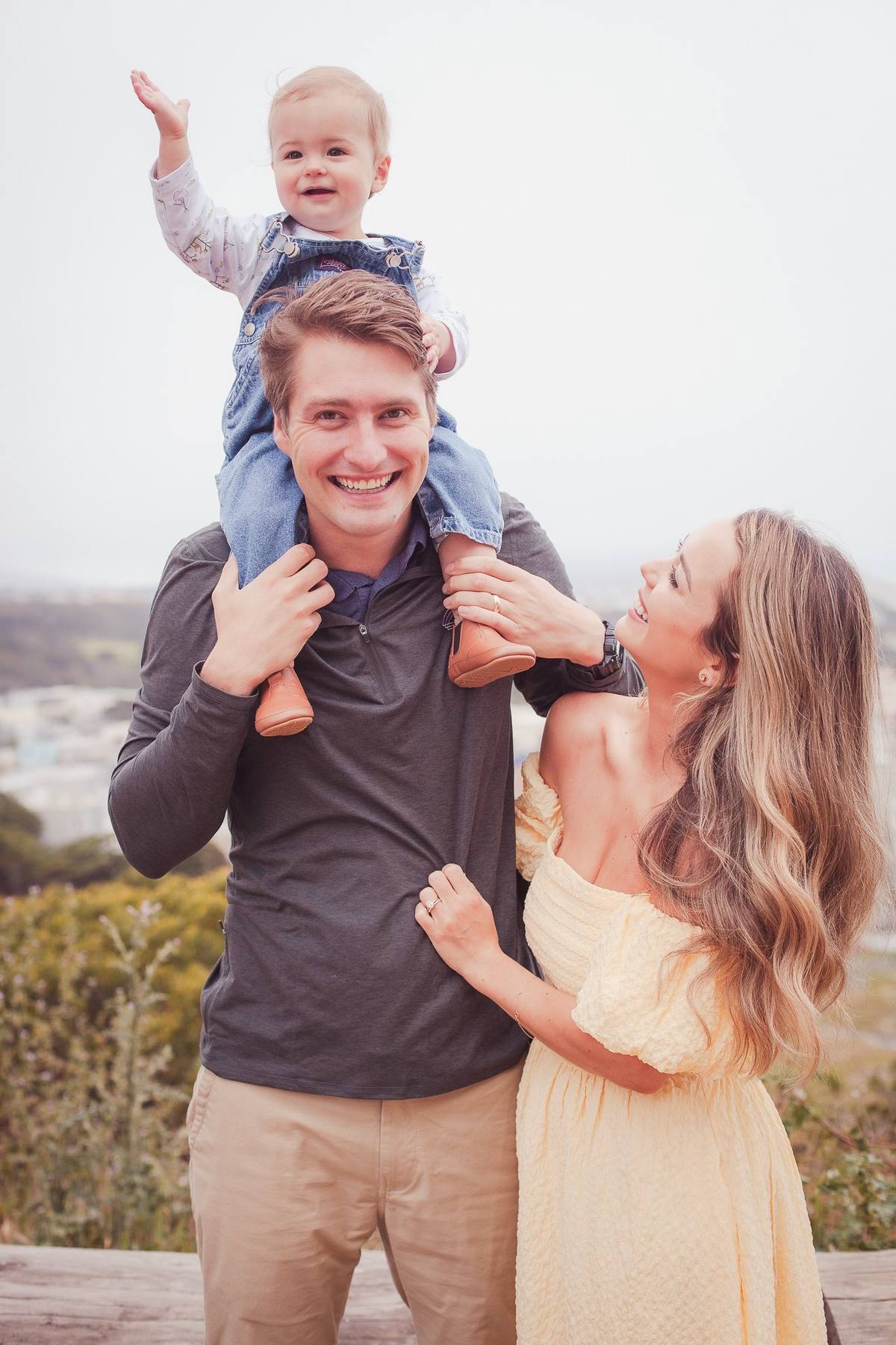 Baby boy waving from his father's shoulders with mom beside them at Sutro Park