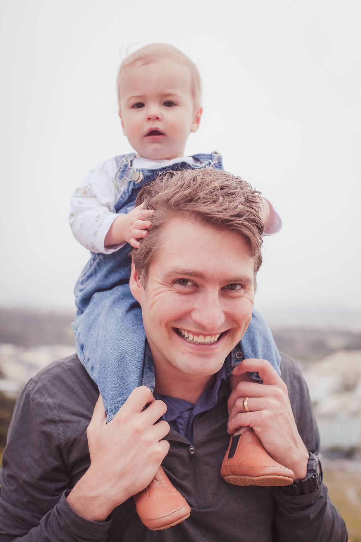 Smiling father with his baby son on his shoulders and the coastline behind them