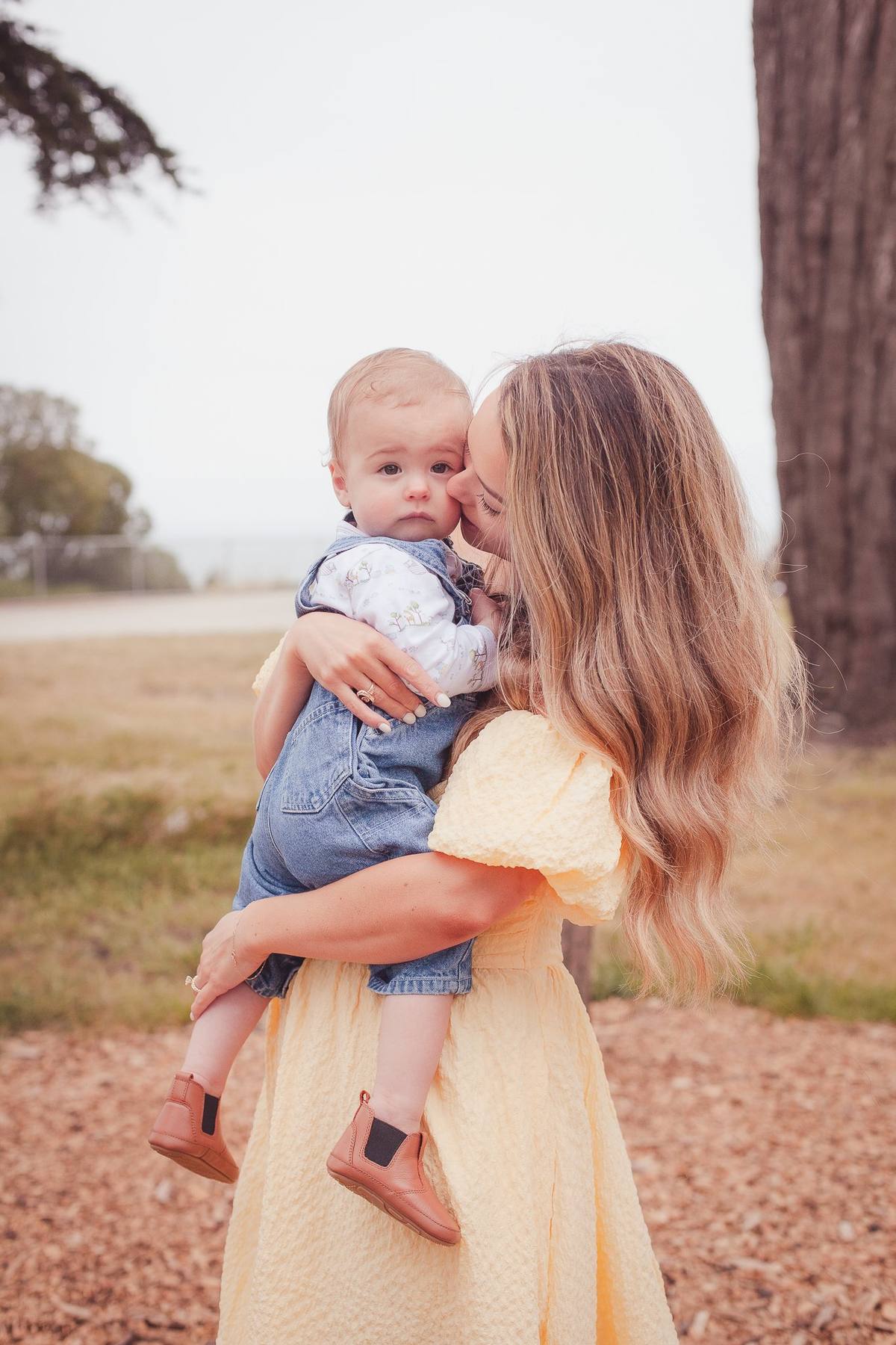 Mother kissing her baby son's cheek as she holds him in a field at Sutro Park