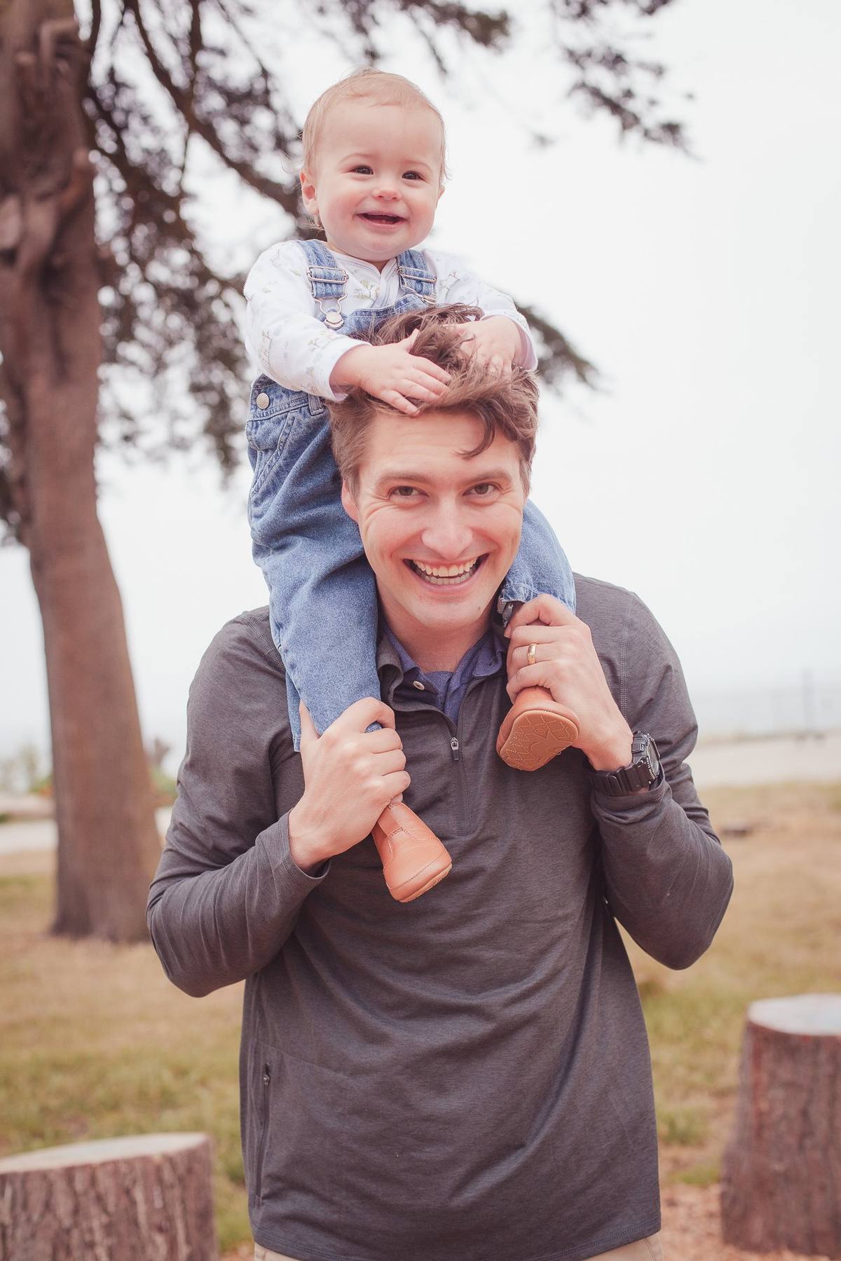 Baby boy grinning on his father's shoulders under a tree at Sutro Park