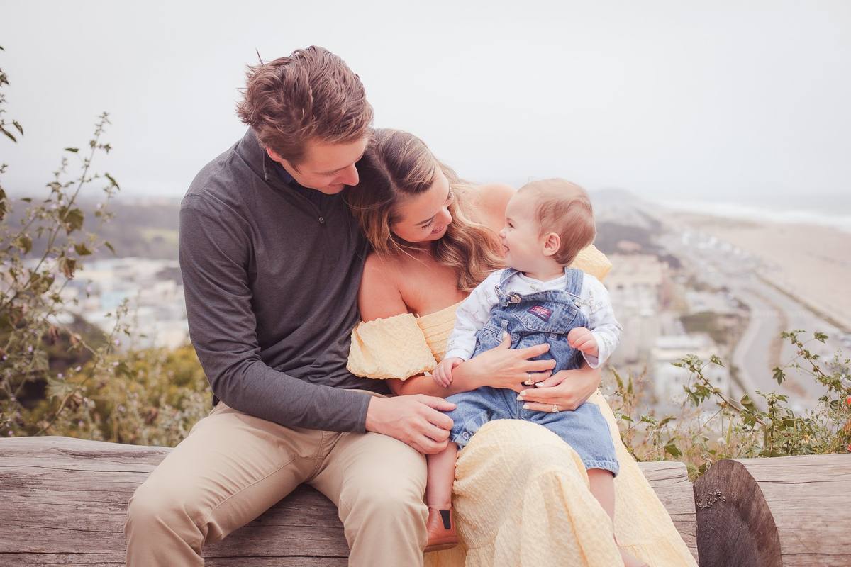 Parents snuggling their baby on a log overlooking Ocean Beach and the Richmond District
