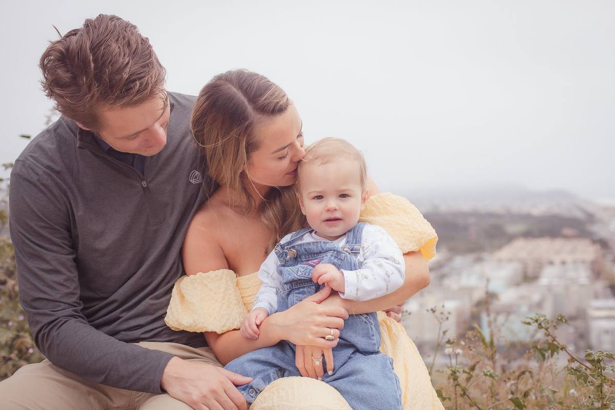 Mother kissing her baby as dad leans in, with the Richmond District in the distance